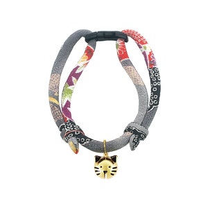 May include: A gray, red, and purple cat collar with a gold cat charm. The collar is made of fabric and has a plastic buckle.