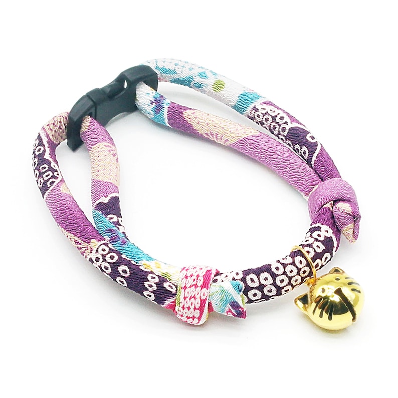May include: A purple and white patterned cat collar with a gold cat bell charm. The collar is adjustable with a black plastic buckle.