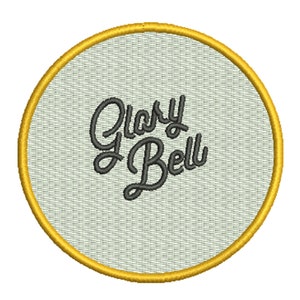 May include: A round, white embroidered patch with a gold border. The patch features the text "Glory Bell" in a black cursive font.