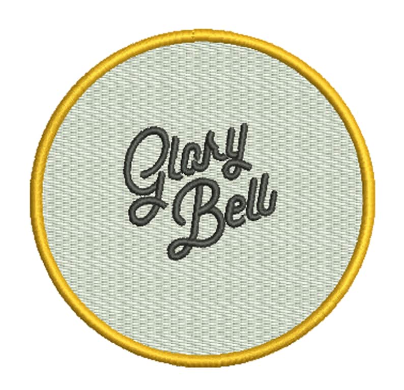 May include: A round, white embroidered patch with a gold border. The patch features the text "Glory Bell" in a black cursive font.