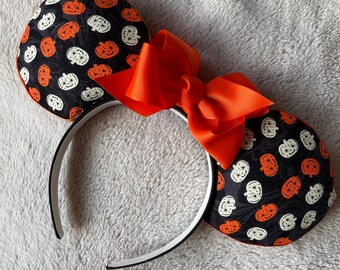 May include: Black headband with white and orange pumpkin print fabric mouse ears and a large orange bow.