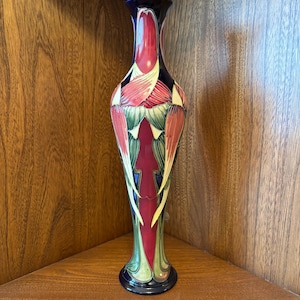 May include: A tall, slender vase with a blue, green, and red floral design. The vase has a narrow neck and a wide base.
