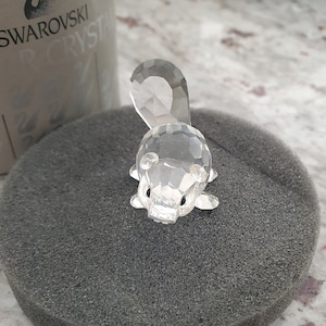 May include: A clear crystal figurine of a squirrel, sitting on a grey foam surface. The figurine is made by Swarovski.
