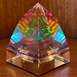 May include: A multi-faceted crystal pyramid with iridescent rainbow colours. The pyramid is made of clear glass and has a square base.