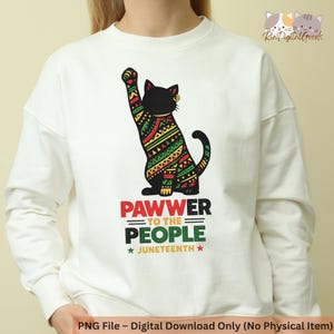 May include: White sweatshirt featuring a black cat with a raised paw, adorned with a colorful geometric pattern in green, red, and yellow. The text "PAWWER TO THE PEOPLE" and "JUNETEENTH" is printed below the cat. A digital download.