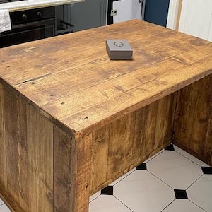 May include: A rustic wooden kitchen island with a natural wood finish. The island has a thick, solid top and a simple, rectangular shape. The island is made of reclaimed wood and has a distressed look.