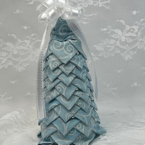 May include: A blue and white fabric Christmas tree with a white bow on top. The tree is decorated with white beads.