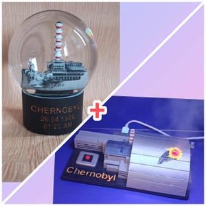 May include: A snow globe featuring a detailed replica of the Chernobyl nuclear power plant, with a red and white striped chimney. The base is black with the word "Chernobyl" and the date and time of the disaster. Next to it is a model of a machine with the word "Chernobyl".