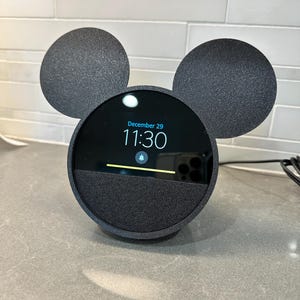May include: Black smart speaker with Mickey Mouse ears, displaying the date December 29 and the time 11:30. The speaker has a notification icon on the screen.