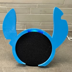 May include: A blue 3D printed case shaped like Stitch from Lilo & Stitch, designed to fit a smart speaker. The case has a light blue accent around the speaker's front.