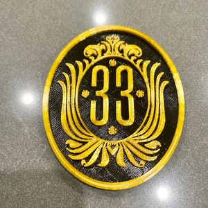 May include: A black and gold round plaque with a decorative design and the number 33 in the center.