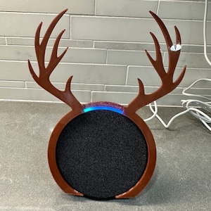 May include: A brown, antler-shaped speaker cover. The cover is designed to fit a round speaker with a black mesh front. The antlers extend upwards, and a blue light glows from the top of the speaker.