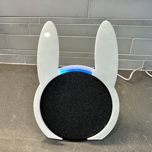 May include: A white bunny-shaped speaker with a black speaker grille and a blue light around the edge.