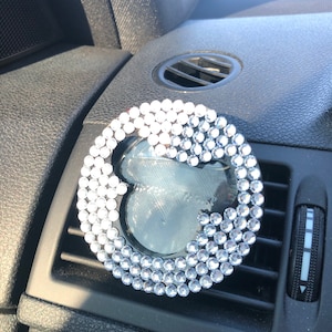 May include: A silver car air freshener with a clear plastic insert and a design of rhinestones in the shape of a heart.