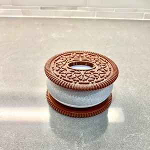 May include: A brown and white cookie-shaped smart speaker with a decorative design on the top.