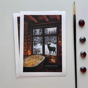 Op de afbeelding: Een rechthoekige kunstdruk met het interieur van een gezellige hut met een dampend bad, brandende kaarsen en een raam met uitzicht op een besneeuwd bos met een hert. De tekst artbynavnita is zichtbaar. Een dunne penseel en vier kleine rode glazen kralen liggen ernaast.