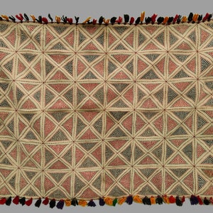 May include: A white cotton textile with a geometric pattern of red, black, and blue triangles. The textile has a fringe border with tassels in various colours.