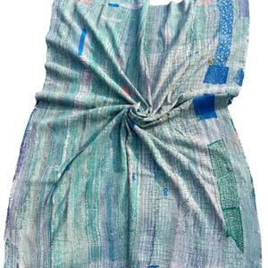 May include: A hand-stitched, textured blanket in shades of blue, green, and white. The blanket features a patchwork design with vertical and horizontal lines, and scattered rectangular patches of darker blue and green. The fabric is soft and appears to be lightweight.