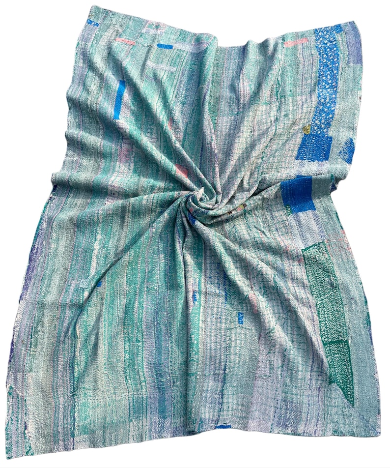 May include: A hand-stitched, textured blanket in shades of blue, green, and white. The blanket features a patchwork design with vertical and horizontal lines, and scattered rectangular patches of darker blue and green. The fabric is soft and appears to be lightweight.