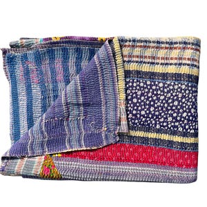 Pode incluir: Um edredom dobrado multicolorido com um design de patchwork. O edredom apresenta vários padrões, incluindo listras e motivos florais, em tons de azul, roxo, vermelho e amarelo. O edredom é feito de um tecido macio e texturizado.
