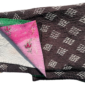 May include: A folded, multi-layered quilt with a variety of colors and patterns. The top layer is dark brown with white diamond-shaped stitching. Other layers include green, pink with floral embroidery, and a light gray quilted fabric.