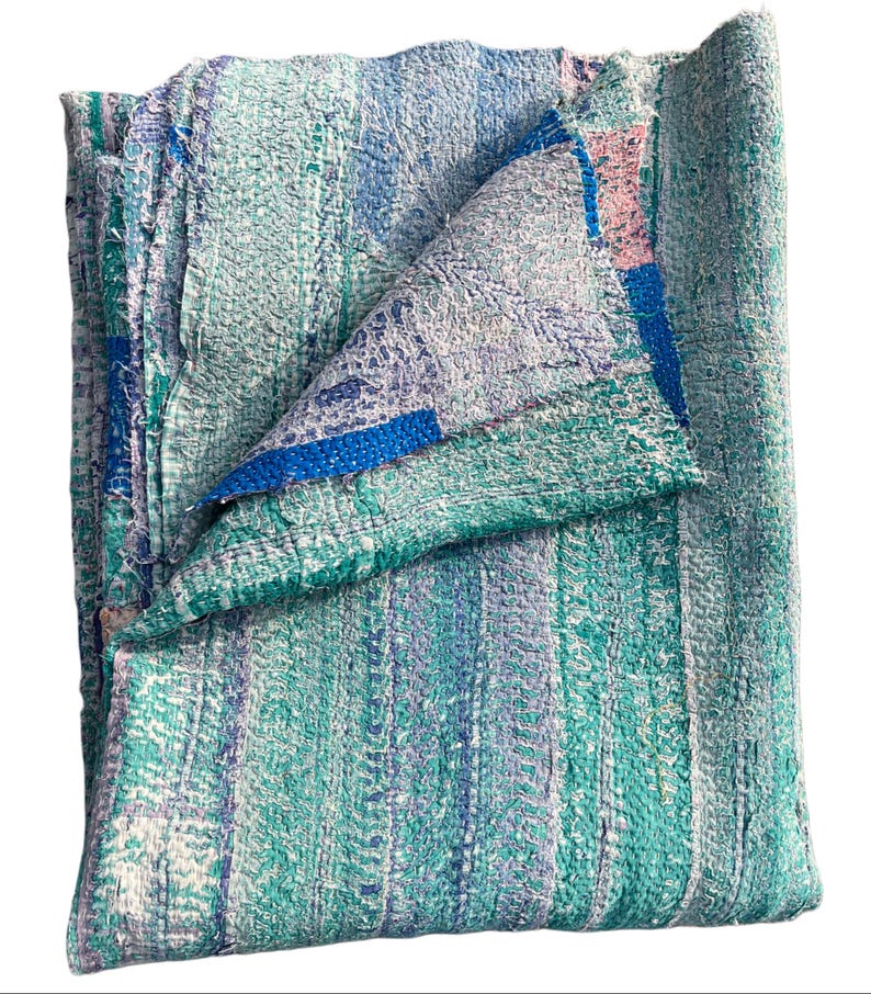 May include: A folded, multi-colored blanket with a textured, stitched appearance. The blanket features vertical stripes in shades of teal, blue, and white, with a folded section revealing a blue border and pink accents. The blanket is made of a soft material.