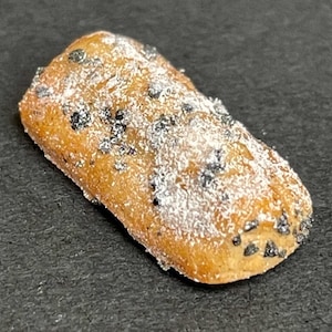 Puede incluir: Un pastel rectangular de color marrón dorado, salpicado de semillas oscuras y espolvoreado con azúcar glas. El postre se presenta sobre una superficie oscura, resaltando su textura y color.