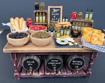 Puede incluir: Un puesto de mercado en miniatura con cuencos de madera llenos de aceitunas negras y verdes, panes y botellas de aceite de vidrio. Tres barriles de madera etiquetados como Olive Oil, Extra Virgin Olive Oil y Balsamic Vinegar.
