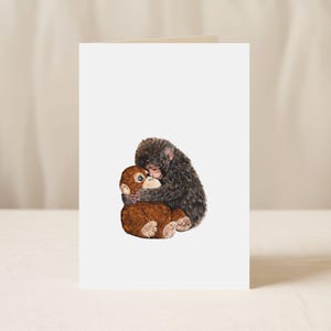 May include: A blank greeting card featuring a watercolor illustration of two monkeys embracing. One monkey is brown, and the other is dark gray. The card is white with a soft, neutral background.