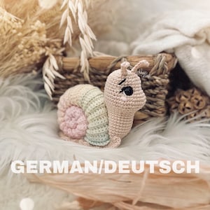 May include: A crocheted snail toy with a rainbow shell. The snail is light pink with black eyes and a small mouth. The shell is made of pink, green, and blue yarn.