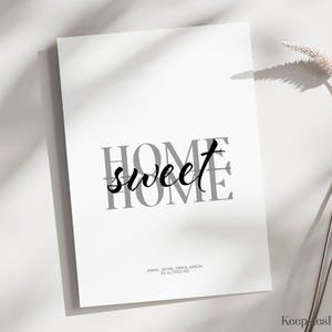 An unframed home sweet home print resting on a surface next to a dried grass stem.
