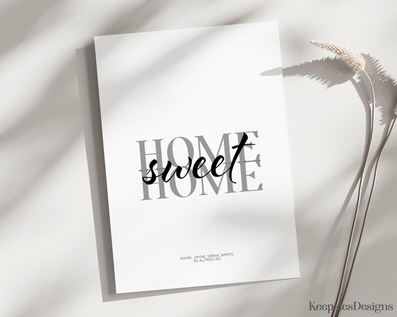 An unframed home sweet home print resting on a surface next to a dried grass stem.