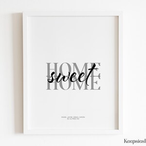 A white framed home sweet home art print hanging on a plain white wall.