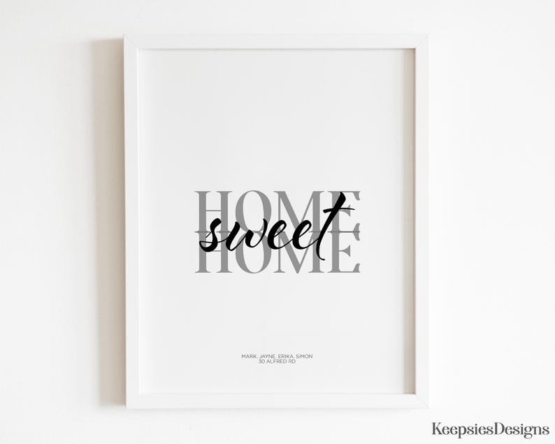A white framed home sweet home art print hanging on a plain white wall.