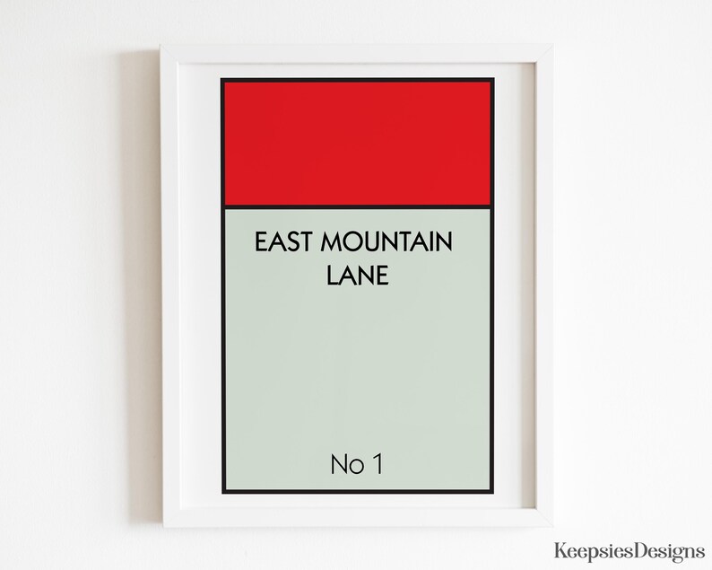 May include: A framed wall art print featuring a rectangular design with a solid red top bar and a light grey lower section. The text EAST MOUNTAIN LANE is printed in black in the centre, with No 1 at the bottom, all enclosed in a white frame.
