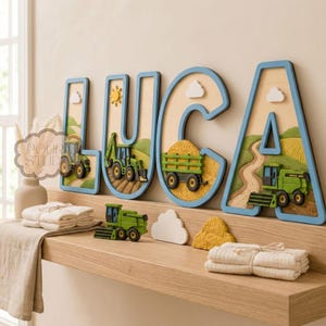 May include: A wooden name sign spelling "LUCA" with a blue border and farm-themed cutouts. Each letter features a different farm scene, including tractors, fields, and clouds. The sign is displayed on a wooden shelf with additional farm-themed decorations.