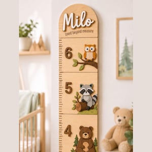 May include: A light wood growth chart featuring the name Milo in white script, the text loved beyond measure, and three-dimensional wooden cutouts of an owl, a raccoon, and a bear next to the numbers 6, 5, and 4 with black measurement markings.