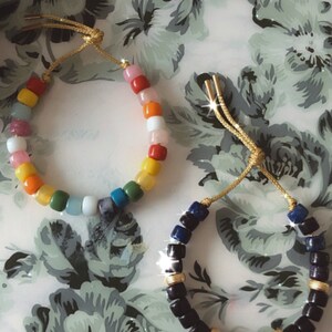 May include: Two bracelets made with colorful beads. One bracelet is made with rainbow colored beads and the other is made with black beads with gold accents.