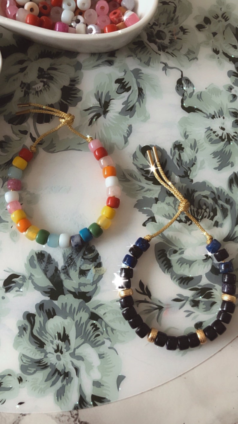May include: Two bracelets made with colorful beads. One bracelet is made with rainbow colored beads and the other is made with black beads with gold accents.