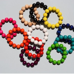 May include: A collection of colorful beaded bracelets in various shades, including pink, orange, red, white, purple, green, blue, yellow, black, and natural wood tones. The bracelets are arranged in a circular shape, showcasing the vibrant colors.