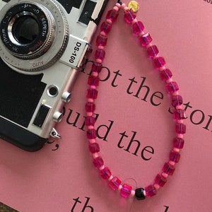 Può includere: Un braccialetto di perline rosa e nero con un ciondolo dorato che dice "TMSI". Il braccialetto è su una superficie rosa con il testo "Ospitalità - l'arte di ricevere, di dare il benvenuto e di guardare... è uno dei principi fondamentali delle lingue e di promuovere fantastiche avventure... non la storia, ma gli ospiti."