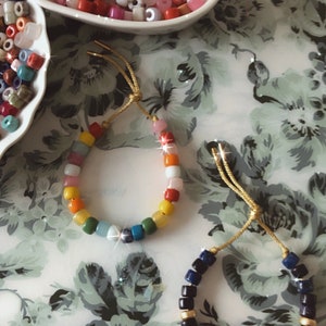 May include: Two bracelets made with colorful beads. One bracelet is made with rainbow colored beads and the other is made with black and blue beads.