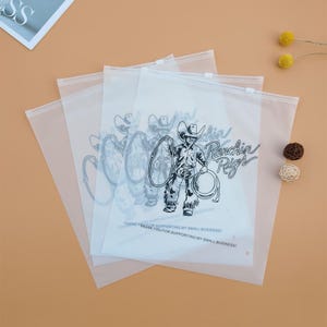 May include: Four clear plastic zippered bags with a black and white cowboy graphic and the text "Ranchin' Rigs" printed on them. The text "Thank you for supporting my small business!" is printed on the bottom of the bags.