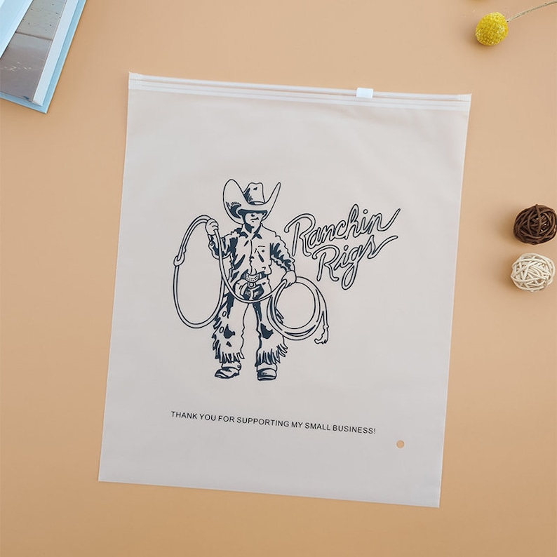 Puede incluir: Una bolsa de pl&aacute;stico blanca resellable con cierre de cremallera. La bolsa tiene una ilustraci&oacute;n en blanco y negro de un vaquero con un lazo y el texto "Ranchin' Rigs" en una fuente estilizada. El texto "Thank you for supporting my small business!" est&aacute; impreso debajo de la ilustraci&oacute;n.