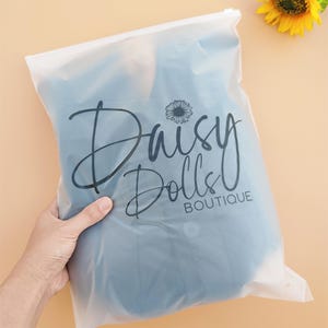 May include: A clear plastic zip-lock bag with a black logo that says "Daisy Dolls Boutique" and a small daisy graphic.