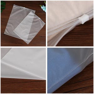 May include: Two clear plastic zippered storage bags, one slightly larger than the other, are laid out on a wooden surface. The bags are made of a thin, translucent material and have a zipper closure along the top edge. The zipper is white and has a small plastic slider.