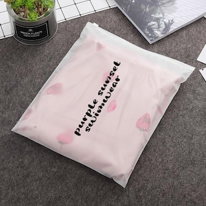 May include: A clear plastic bag with a zipper closure. The bag contains a pink swimsuit with a floral print and the text "purple sunset swimwear" printed on the front.