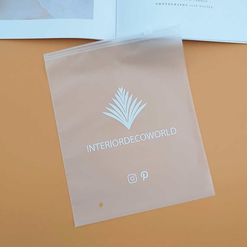 Puede incluir: Una bolsa de pl&aacute;stico transparente con cierre de cremallera. La bolsa tiene un logotipo blanco que dice "INTERIORDECOWORLD" con un dise&ntilde;o de palmera estilizado sobre el texto. El logotipo tambi&eacute;n incluye iconos de redes sociales para Instagram y Pinterest.