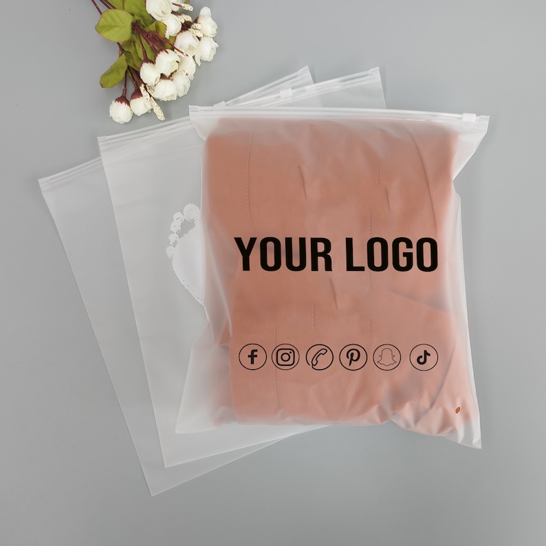 Puede incluir: Bolsas transparentes de pl&aacute;stico con cierre de cremallera. Las bolsas tienen un logotipo impreso que dice "YOUR LOGO" y iconos de redes sociales para Facebook, Instagram, un tel&eacute;fono, Pinterest, Snapchat y TikTok.