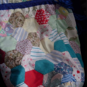 May include: A patchwork quilt with a hexagonal pattern in various colours, including blue, green, red, and white. The quilt is made of different fabrics and textures, creating a unique and colourful design.
